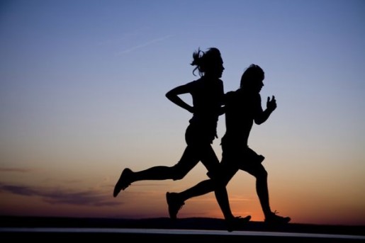 Young couple: man and  woman run together on a sunset on lake coast.  Silhouette.